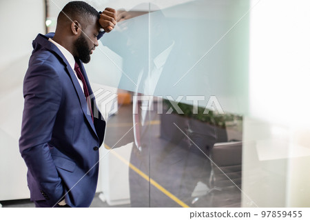Exhausted black businessman leaning on window glass 97859455