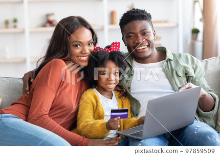 Happy Black Family With Laptop And Credit Card Relaxing At Home 97859509