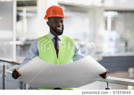 Cheerful black civil engineer in safety workwear holding draft 97859688