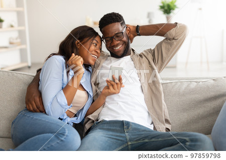 African american couple sitting on couch, using cellphone African american couple sitting on couch, using cellphone 97859798