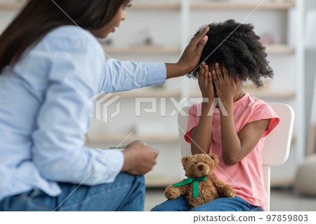 African american woman comforting emotional curly girl preschooler, clinic interior 97859803