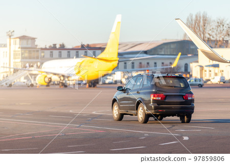 Scenic view of airport security car on tarmac apron taxiway in warm sunlight of bright morning sunrise or evening sunset time. Follow me safety vehicle staff. Aviation maintenance and service machine 97859806