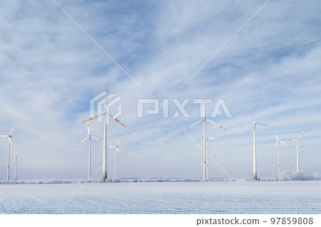 Scenic landscape view of white snowy frosty field and big modern wind turbine mill farm against beautiful blue clouds blue sky. All season clean green renewable sustainable energy generation concept Scenic landscape view of white snowy frosty field and big modern wind turbine mill farm against beautiful blue clouds blue sky. All season clean green renewable sustainable energy generation concept 97859808