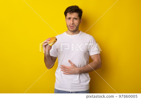 Sad Young Guy Holding Burger Suffering From Stomachache 97860005