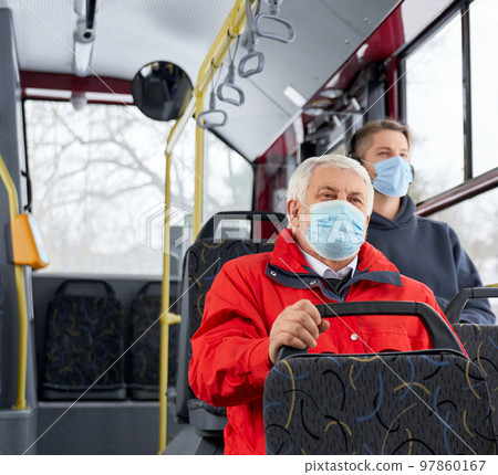 Passengers protecting by medical masks traveling by public transpost, sitting on bus. People going by bus home, old man and brunette man sitting, looking. Concept of pandemic. 97860167