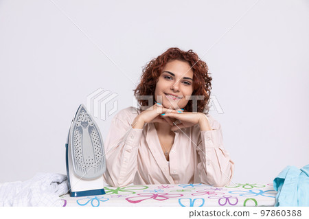 A smiling woman sits at the ironing board and iron. A smiling woman sits at the ironing board and iron. 97860388