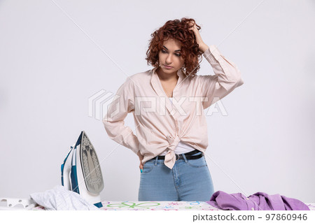 The girl stands over the ironing board and wonders when it will all be done. The girl stands over the ironing board and wonders when it will all be done. 97860946
