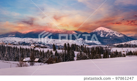 Alpine village outskirts panorama in last evening sunset sun light. Winter snowy hills and fir trees, magnificient and picturesque mountain range in far. Voronenko, Ukraine, Carpathian. Alpine village outskirts panorama in last evening sunset sun light. Winter snowy hills and fir trees, magnificient and picturesque mountain range in far. Voronenko, Ukraine, Carpathian. 97861247
