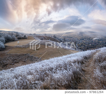 Winter coming. Picturesque pre sunrise scene above late autumn mountain countryside with hoarfrost on grasses, trees, slopes. Peaceful sunlight rays from cloudy sky. Ukraine, Carpathian Mountains. Winter coming. Picturesque pre sunrise scene above late autumn mountain countryside with hoarfrost on grasses, trees, slopes. Peaceful sunlight rays from cloudy sky. Ukraine, Carpathian Mountains. 97861264