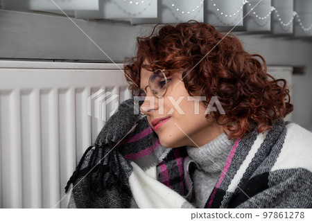 A girl huddled around a hot radiator. The first start of the central heating system. A girl huddled around a hot radiator. The first start of the central heating system. 97861278