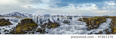 Season changing in southern Highlands of Iceland. Picturesque waterfal Tungnaarfellsfoss panoramic autumn view.  Landmannalaugar mountains under snow cover in far. 97861376