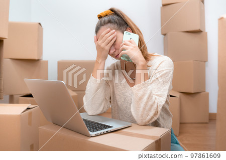 Caucasian woman with headache from moving to new home with laptop and talks to consultant on phone. 97861609