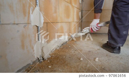 A worker sprays putty on a wall. The process of applying plaster to walls inside a building by machine. Applying plaster on the wall using equipment. 97861656