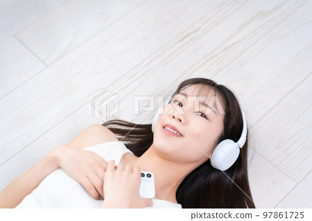 一個躺在地板上沉浸在智能手機音樂中的女人 97861725