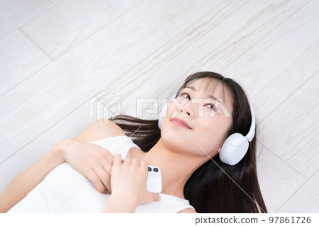 A woman lying on the flooring and immersed in smartphone music A woman lying on the flooring and immersed in smartphone music 97861726