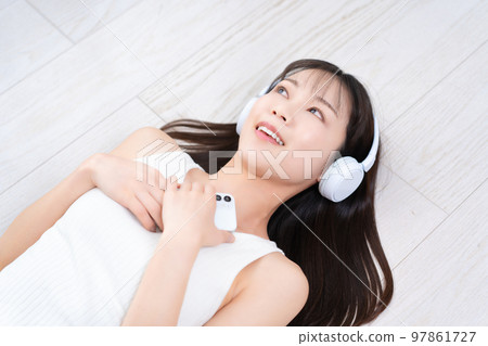 A woman lying on the flooring and immersed in smartphone music A woman lying on the flooring and immersed in smartphone music 97861727
