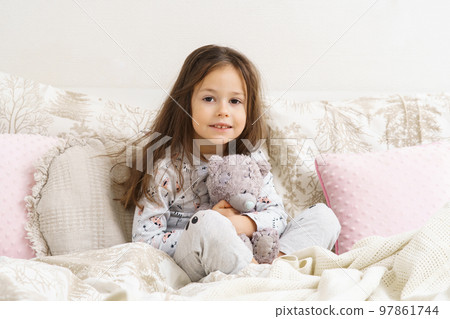 Little girl smiling with sleepy eyes and hugging favorite stuffed toy. Resting on cozy bed, waking up at morning. Little girl smiling with sleepy eyes and hugging favorite stuffed toy. Resting on cozy bed, waking up at morning. 97861744
