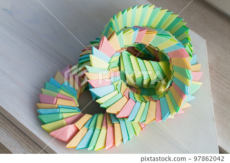 Colorful origami rings lay on a white wooden table, abstract photo 97862042