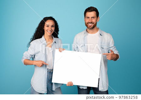 Happy young middle eastern wife and european bearded husband show finger on banner with blank space 97863258