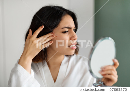 Sad young woman suffering from acne, checking skin in mirror Sad young woman suffering from acne, checking skin in mirror 97863270