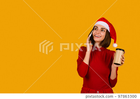 Chreerful young woman in Santa hat having phone conversation Chreerful young woman in Santa hat having phone conversation 97863300