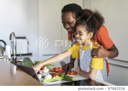 Black Girl Checking Recipe On Digital Tablet While Cooking With Dad 97863356