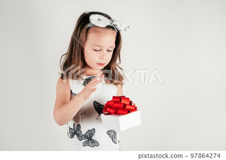 Nice little girl hold present box with bow looking down. Portrait of child on white. Saint Valentine's Day concept. Nice little girl hold present box with bow looking down. Portrait of child on white. Saint Valentine's Day concept. 97864274
