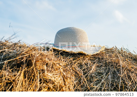 Wicker female panama hat lying at top of haystack. Beautiful clear blue sky. Pile of dry grass. Countryside lifestyle. Wicker female panama hat lying at top of haystack. Beautiful clear blue sky. Pile of dry grass. Countryside lifestyle. 97864513
