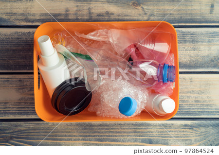 Orange plastic container box full of plastic jar, caps, pellicle and cup rubbish on wooden background. Greenhouse effect Orange plastic container box full of plastic jar, caps, pellicle and cup rubbish on wooden background. Greenhouse effect 97864524