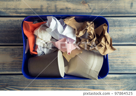 Blue plastic container box full of crumpled paper waste, rubbish on wooden background. Global warming prevention, crisis Blue plastic container box full of crumpled paper waste, rubbish on wooden background. Global warming prevention, crisis 97864525