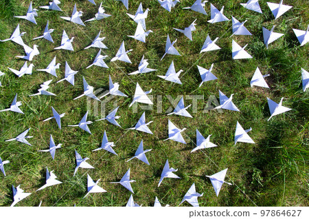 Japanese folded Origami cranes on fresh grass. Hundreds handmade paper birds on green field with copy space. 1000 thousand crane tsuru sculpture topic. Symbol of peace, faith, health, wishes and hope  97864627