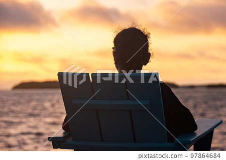Young woman sits on the beach and enjoys the sunset over the sea 97864684
