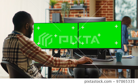 African american man analyzing greenscreen on multi monitors, working in creative agency studio. Male employee looking at isolated display with chroma key copyspace on computer. African american man analyzing greenscreen on multi monitors, working in creative agency studio. Male employee looking at isolated display with chroma key copyspace on computer. 97865335
