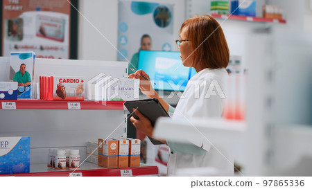 Asian employee giving box of medicine to young man, helping client and working on supplies inventory. Pharmacist analyzing packages of medicaments and showing drugs to customer. Asian employee giving box of medicine to young man, helping client and working on supplies inventory. Pharmacist analyzing packages of medicaments and showing drugs to customer. 97865336