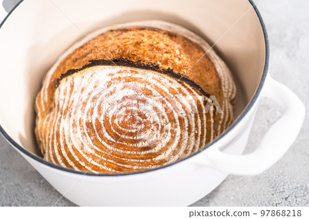 Freshly baked loaf of a wheat sourdough bread with marks from bread proofing basket in enameled cast iron dutch oven. Freshly baked loaf of a wheat sourdough bread with marks from bread proofing basket in enameled cast iron dutch oven. 97868218