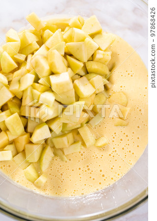 Mixing ingredients in a large glass mixing bowl to bake apple sharlotka muffin. Mixing ingredients in a large glass mixing bowl to bake apple sharlotka muffin. 97868426