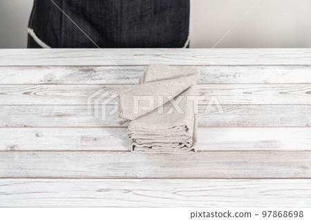 Folding a natural color linen dinner napkin on a white wooden table. Folding a natural color linen dinner napkin on a white wooden table. 97868698