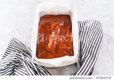 Glazing classic meatloaf with sweet glaze in a loaf pan lined with parchment paper. Glazing classic meatloaf with sweet glaze in a loaf pan lined with parchment paper. 97868720