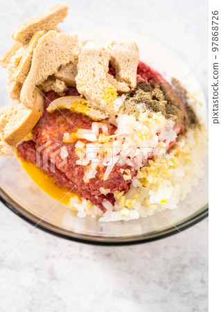 Mixing ingredients with hands in a glass mixing bowl to make meatloaf. Mixing ingredients with hands in a glass mixing bowl to make meatloaf. 97868726