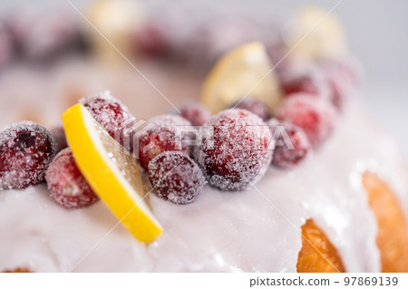Lemon cranberry bundt cake decorated with sugar cranberries and lemon wedges on a cake stand. 97869139