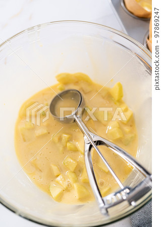 Scooping dough into the cupcake pan lined with parchment muffin liners to bake sharlotka muffins. Scooping dough into the cupcake pan lined with parchment muffin liners to bake sharlotka muffins. 97869247