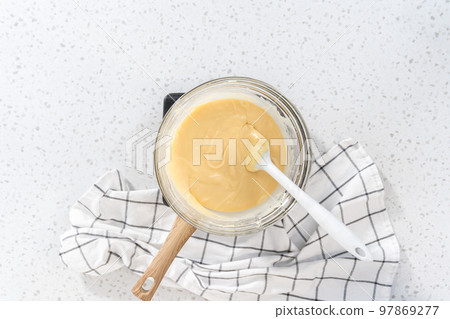 Flat lay. Melting white chocolate chips and other ingredients in a glass mixing bowl over boiling water to prepare white chocolate cranberry pecan fudge. 97869277