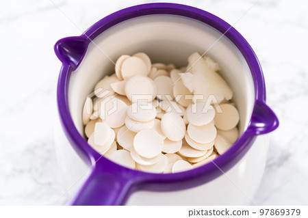 Melting chocolate chips in a candy melting pot to make red, white, and blue chocolate-covered pretzel twists. 97869379