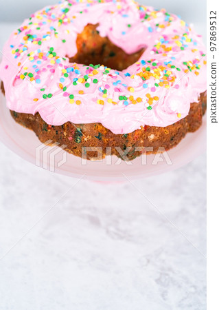 Funfettti bundt cake frosted with pink vanilla buttercream frosting and decorated with rainbow sprinkles. 97869512