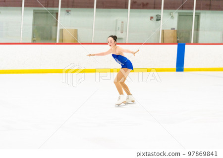 Teenage girl practicing figure skating on an indoor ice skating rink. 97869841