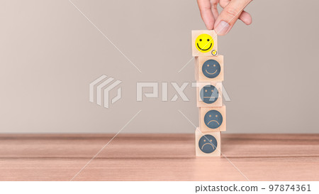 Hand putting a wooden cube block with a smile face icon on wood table. Concept of customer services best excellent business rating experience and testimonial. 97874361