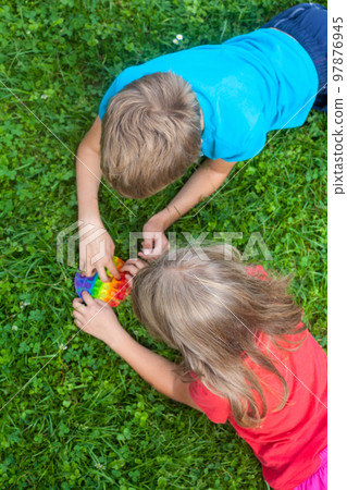 Kids playing with pop it toy on the grass. 97876945
