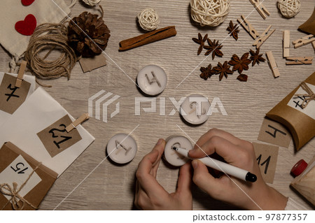 Unrecognizable young woman paint numbers on tea candles. Female making homemade advent calendar Made with your own hands step by step DIY crafts do it yourself. Preparation to christmas concept 97877357