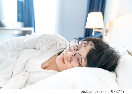 Asian young woman is sleepping on white clean bed in white t-shirt long arm pajamas and in spite of wear glasses on her eyes. Asian young woman is sleepping on white clean bed in white t-shirt long arm pajamas and in spite of wear glasses on her eyes. 97877593