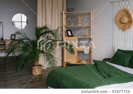 Bedroom interior in Scandinavian style. A bed with green linens, a potted date palm houseplant on the floor 97877758